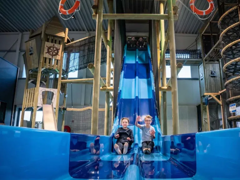 Twee kinderen onderaan de blauwe glijbaan in de binnenspeeltuin van Landal Esonstad