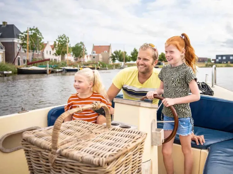 Vader en twee kinderen varen met een sloep door het water langs de huizen van Landal Esonstad