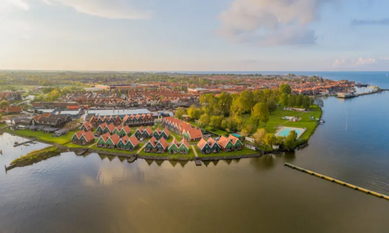 Luchtfoto van de vakantiehuizen aan het water op Landal Volendam, met het buitenzwembad en het dorp erachter